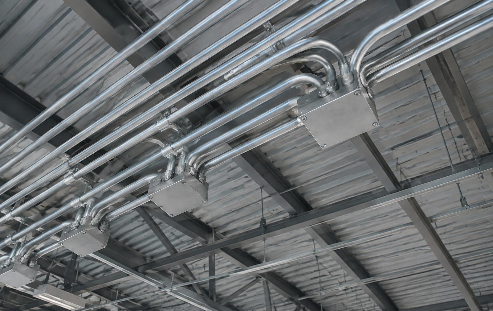 Parallel runs of galvanized electrical conduit and junction boxes across a warehouse ceiling